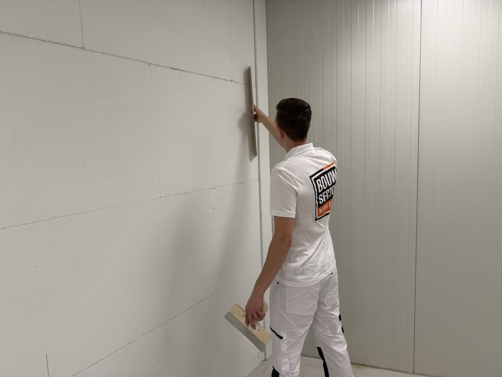 Stukadoor van Bouwsector Nederland met spaan en plamuurmes controleert of een wand vlak is