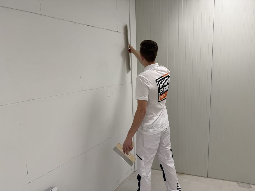 Stukadoor van Bouwsector Nederland trekt met een lange spaan een wand van gipsblokken verticaal vlak